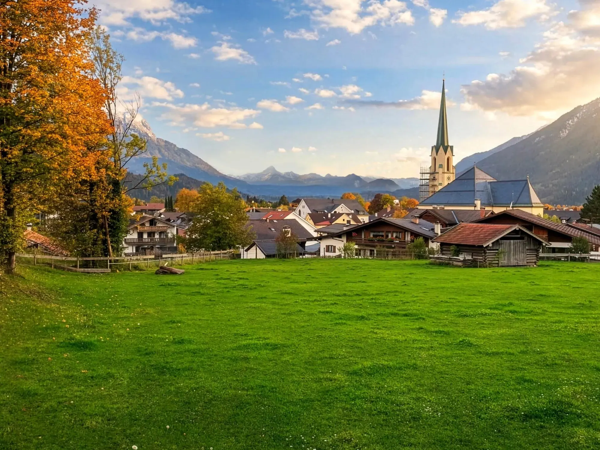 Blick über die Wiese auf Partenkirchen mit Kirchturm, dahinter das Wettersteingebirge im Herbstlicht